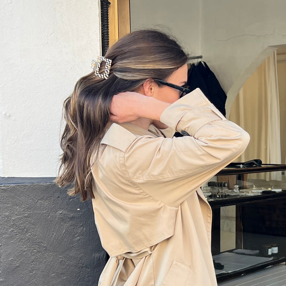 image of girl wearing our square hair claw in daydream in a half-up half-down style. She is wearing a coat and black sunglasses. She is pictured in front of a shop and is lifting her hair up with her hands. 