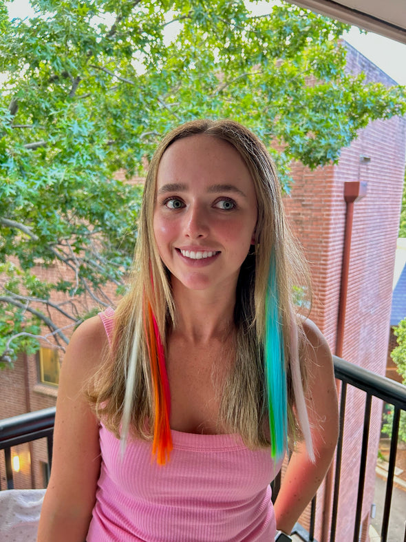Girl wearing clip in hair extensions in orange, yellow, pink, blue and green.