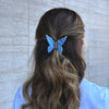 Girl wearing the blue butterfly hair claw in a half-up half-down hairstyle. She is wearing a white t-shirt.