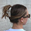 Girl wearing her hair up in our go-to claw in daydream. She is wearing sunglasses, gold earrings and a white t-shirt.