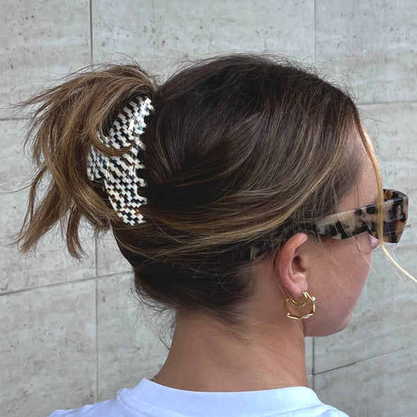 Girl wearing her hair up in our go-to claw in daydream. She is wearing sunglasses, gold earrings and a white t-shirt.