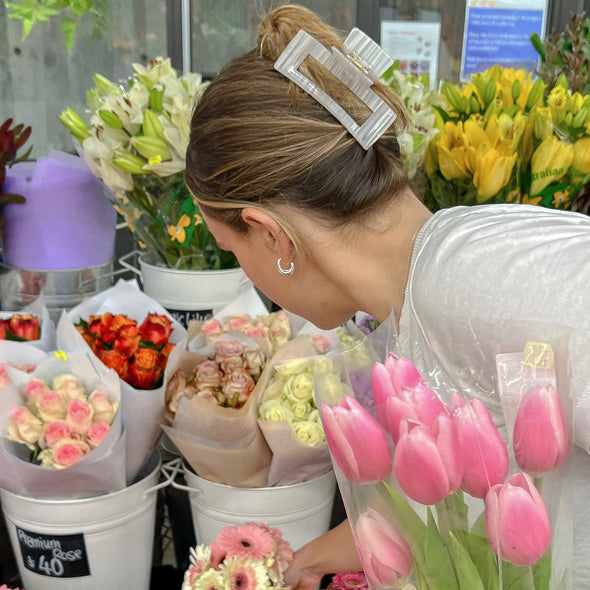Image of girl wearing our classic claw in white. The girl is in a flower shop and is holding pink tulips.