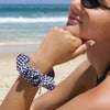 Lady in beach wearing Black - Picnic 4 2 Scrunchie. Colour/Pattern: Black and white gingham. Material: Cotton. Dimensions: Material width approximately 4cm. Made by us in Bondi Beach.