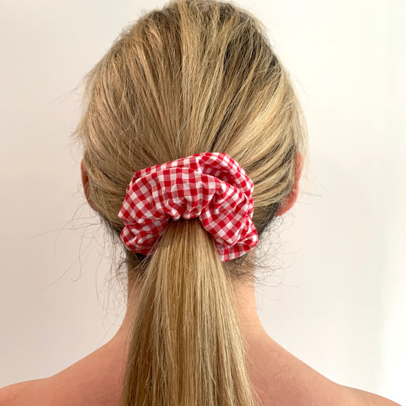 Girl wearing red - Picnic 4 2 Scrunchie. Colour/Pattern: Red and white gingham. Material: Cotton. Dimensions: Material width approximately 4cm. Made by us in Bondi Beach.