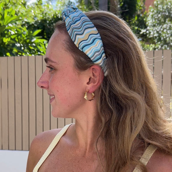 Lady wearing headband in horizontal colours of blues, greys, white and mustard.  Knotted top.
