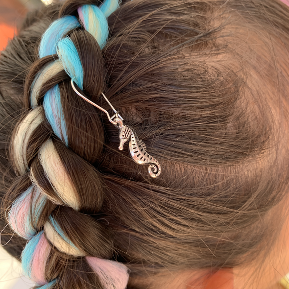 Girl wearing seahorse charm/hair charm in silver colour (hook included). Dimensions: 19mm x 9mm. Material: Charm - zinc alloy, lead free. Hooks - surgical steel.