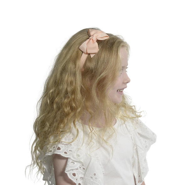Girl wearing pale apricot headband with bow.